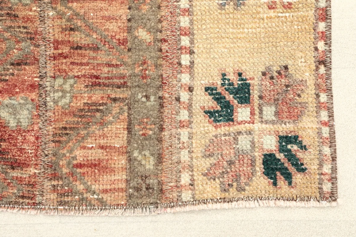 Close-up detail of the rug's end, showing the beige panel with tribal motifs and the central rust stripe.