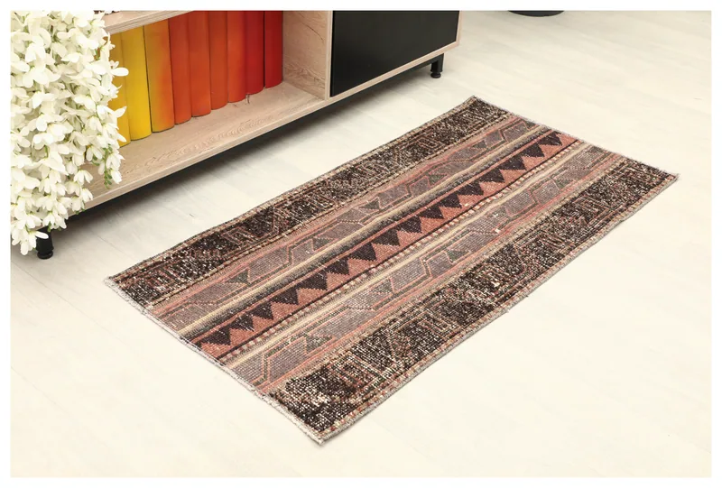 Full top view of the brown and rust geometric Anatolian rug on a white floor next to a bookshelf.