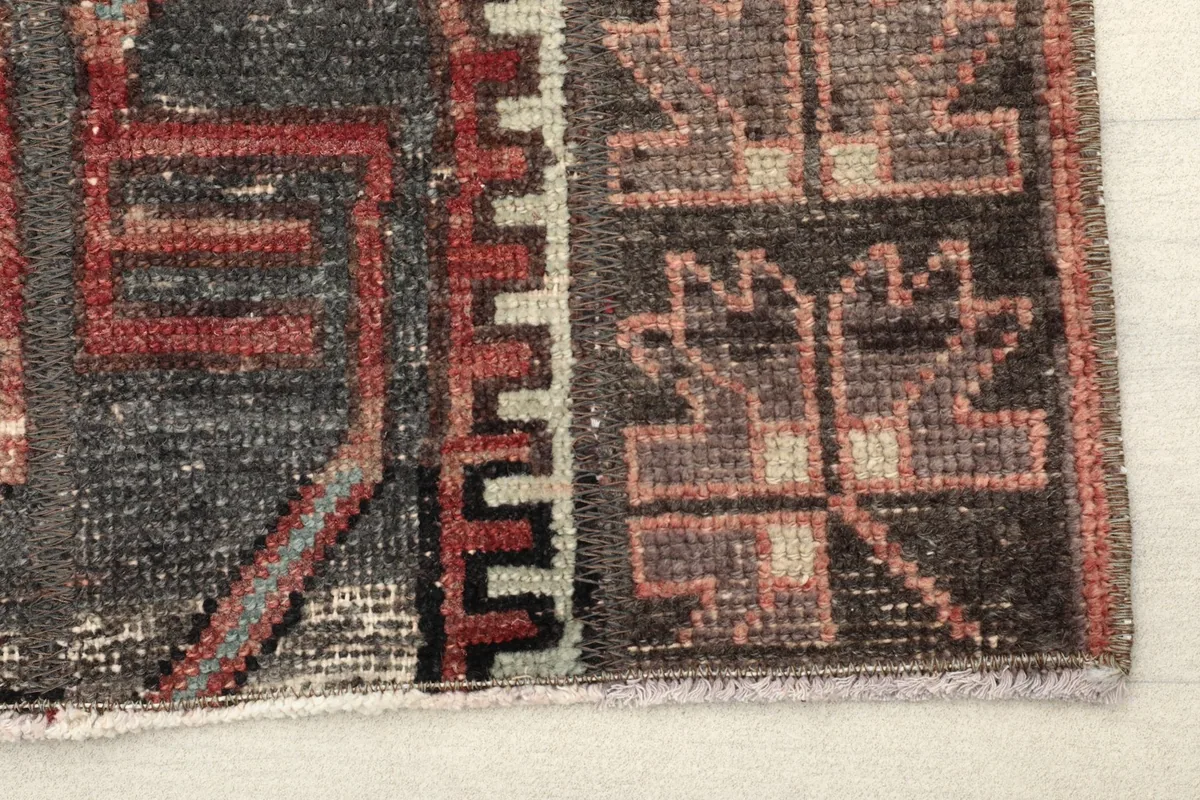 Close-up detail of the charcoal field with rust, red, and beige geometric motifs and border