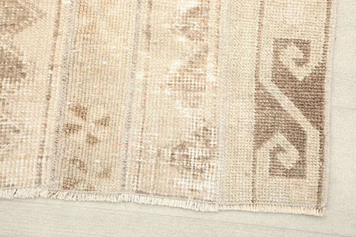 Close-up detail of the rug's low pile and hand-knotted texture, showing beige and brown geometric motifs.