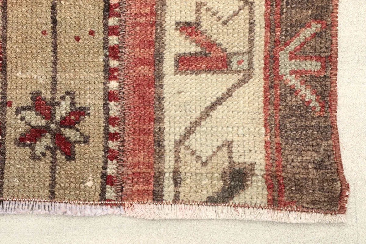 Close-up detail of the rug's texture, showing tan, red, and brown hues with geometric motifs