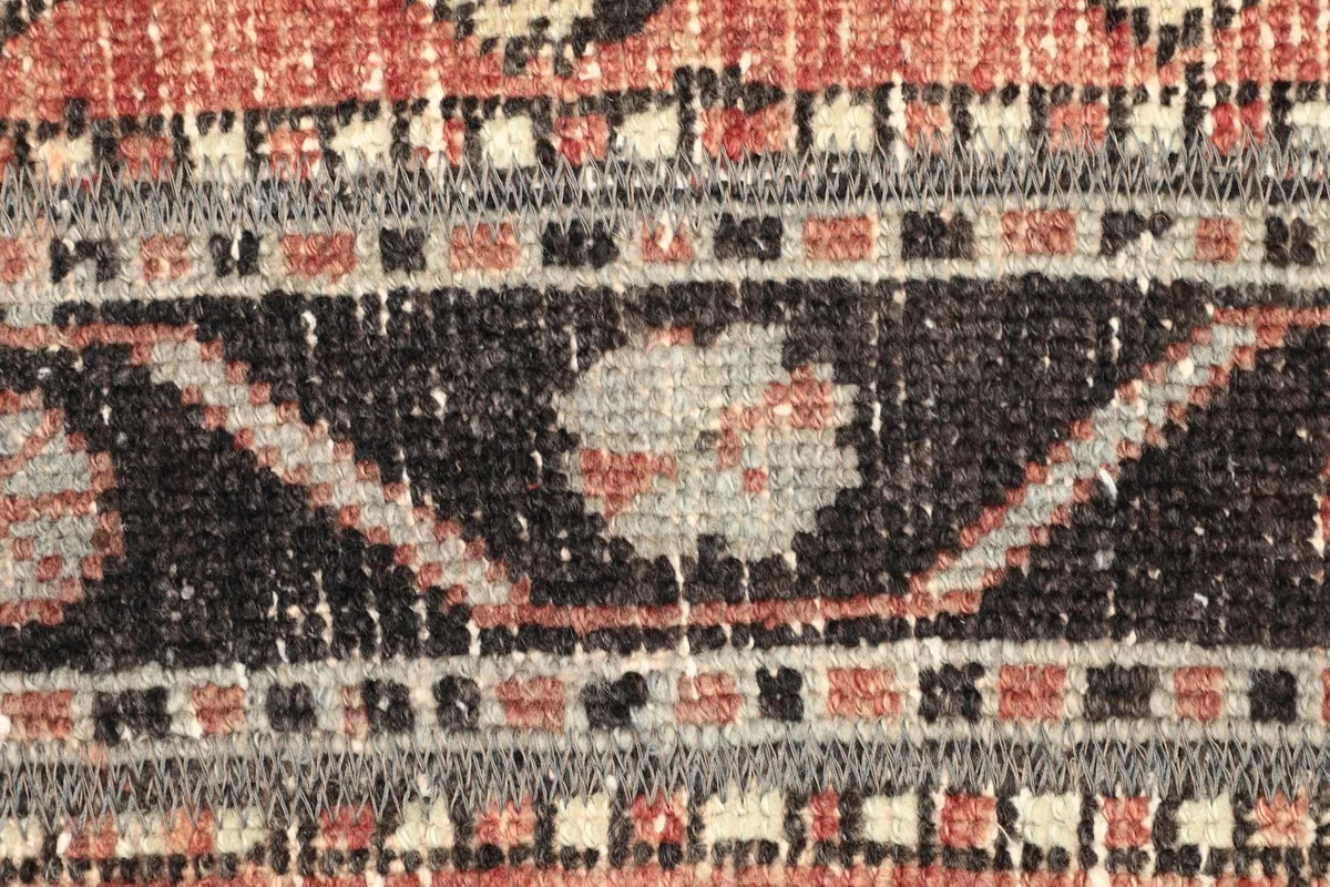 Macro detail of the hand-knotted wool pile, showing the texture and faded rust, black, and beige motifs.