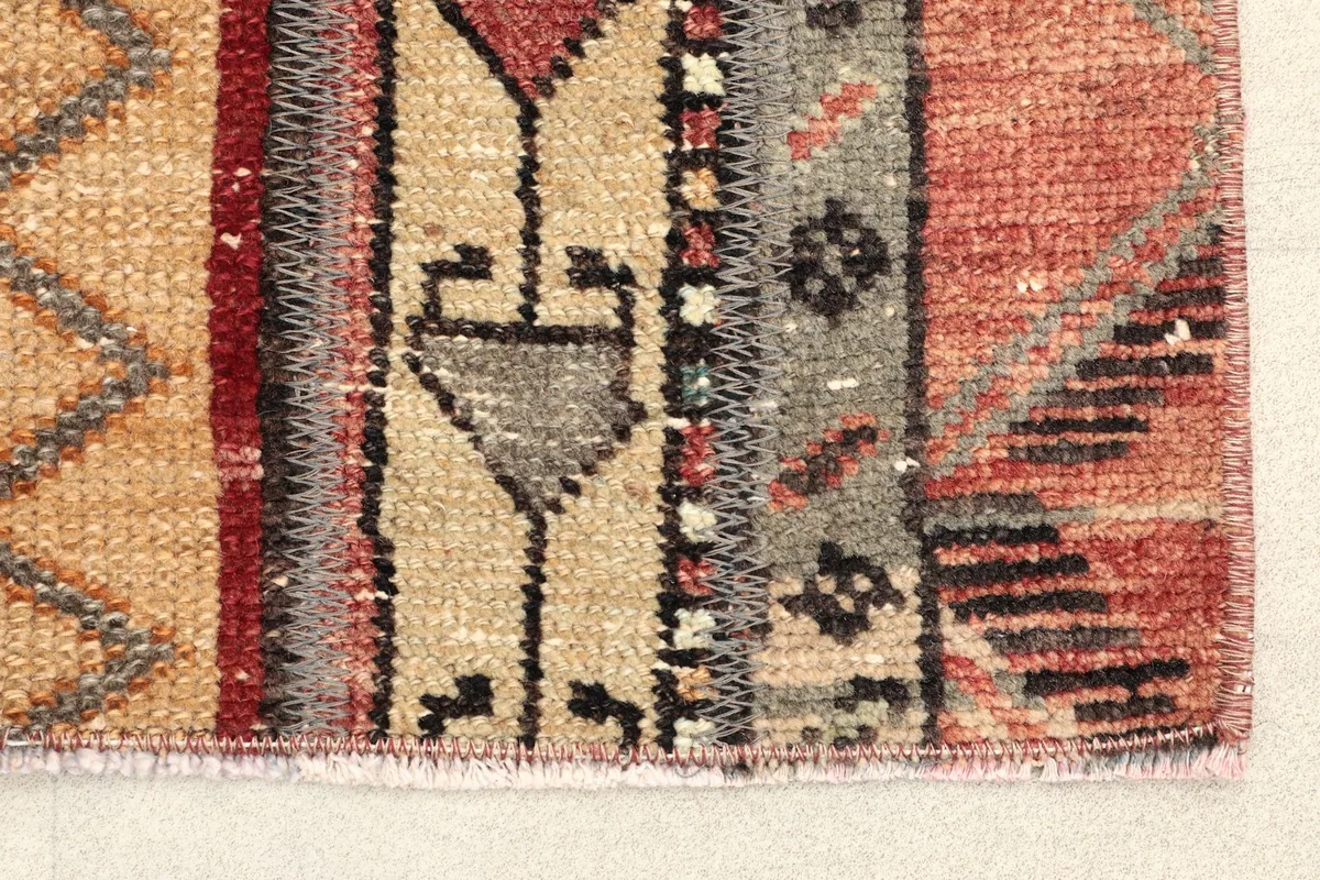 Close-up detail of the rug's edge, showing the beige, red, and gray geometric motifs and texture.
