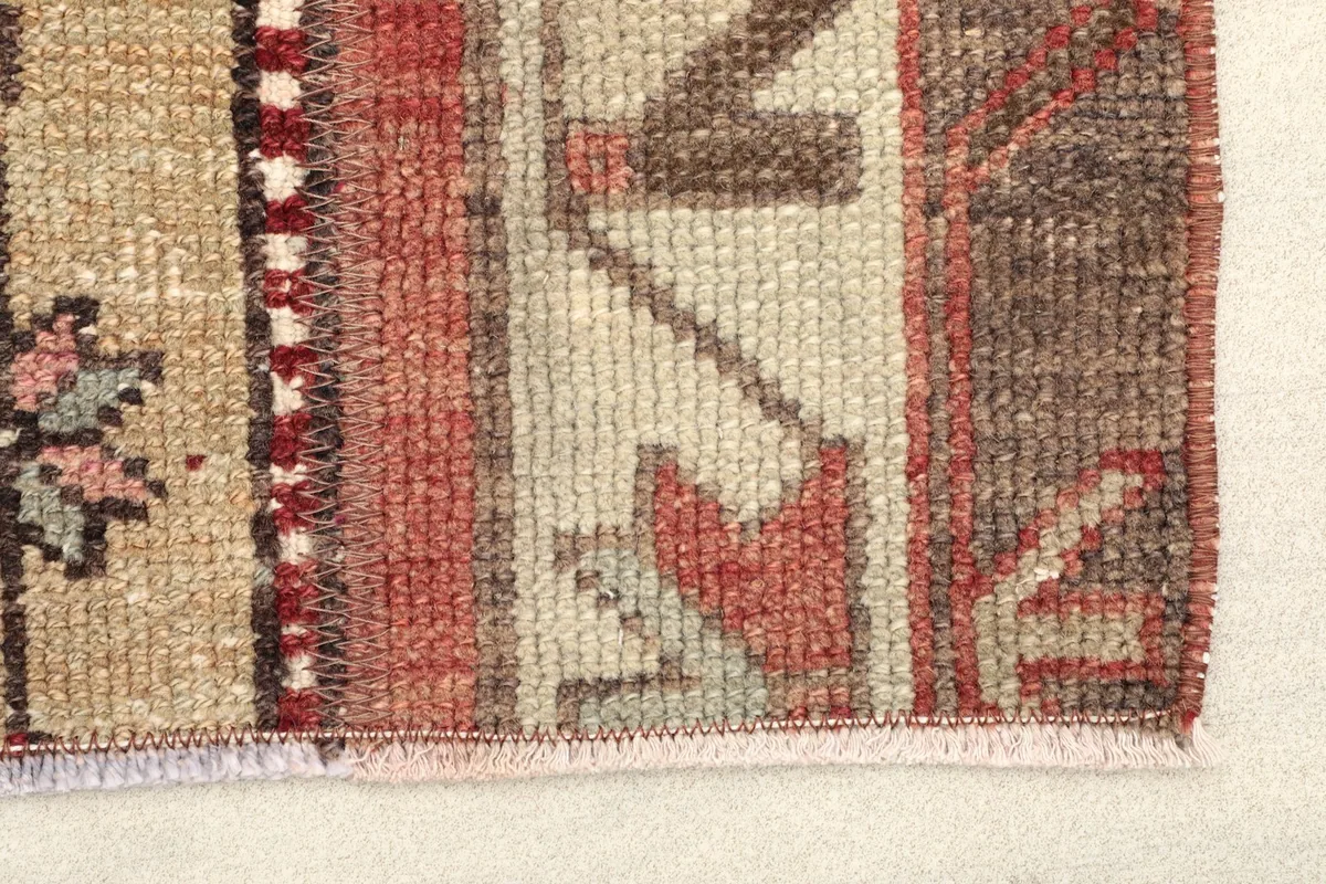 Close-up of the rug's edge, showing the low wool pile and the intricate weaving of the red and tan colors.