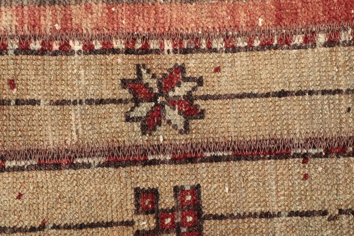 Detailed shot of a floral-like tribal motif in red and brown against the tan field, showcasing the knots.