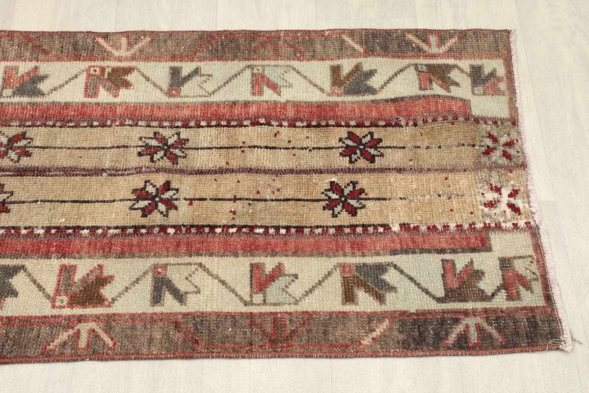 View of the rug's side border, featuring repeating geometric shapes in red, brown, and ivory.