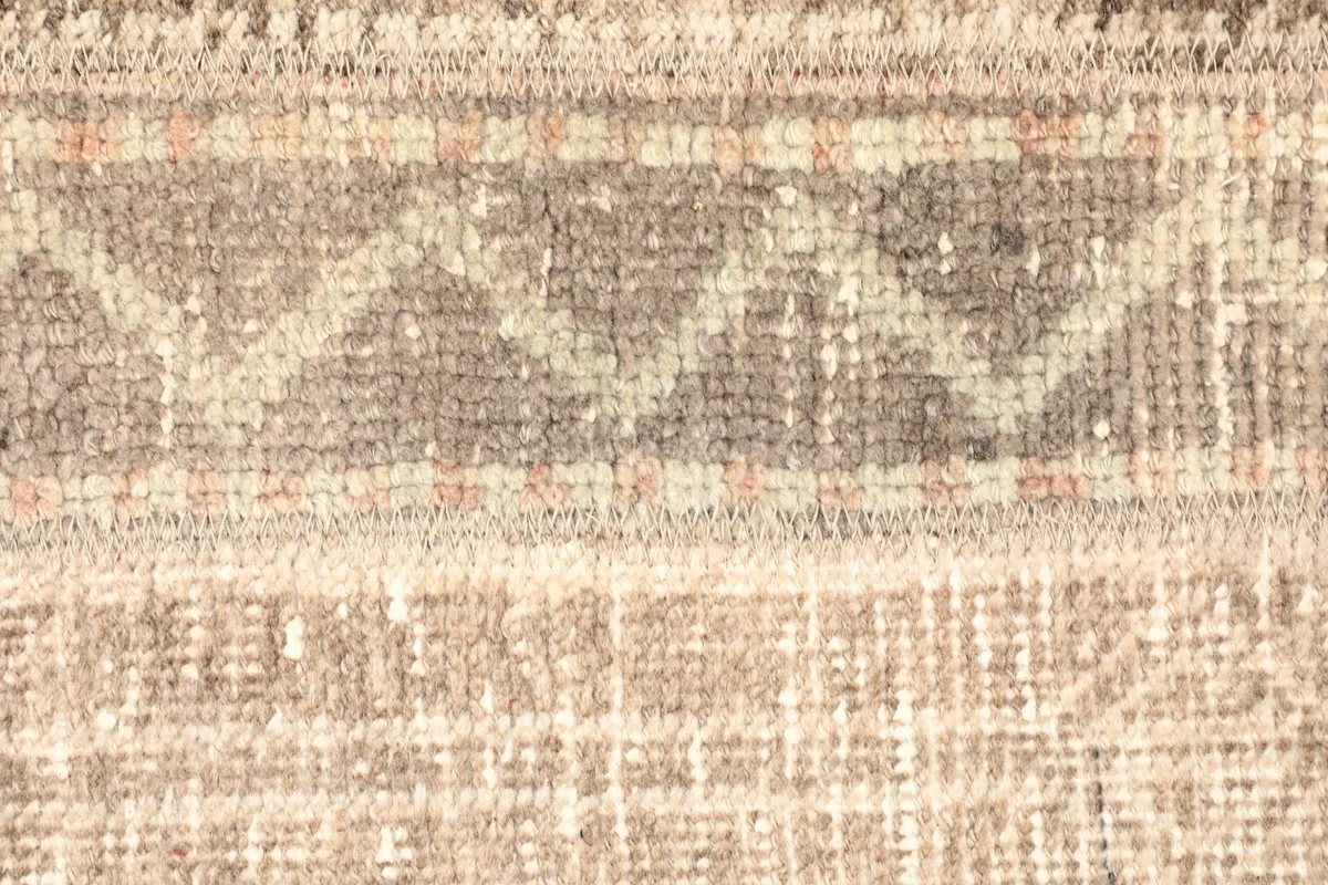 Macro detail of the hand-knotted construction and individual wool fibers in beige, brown, and gray tones