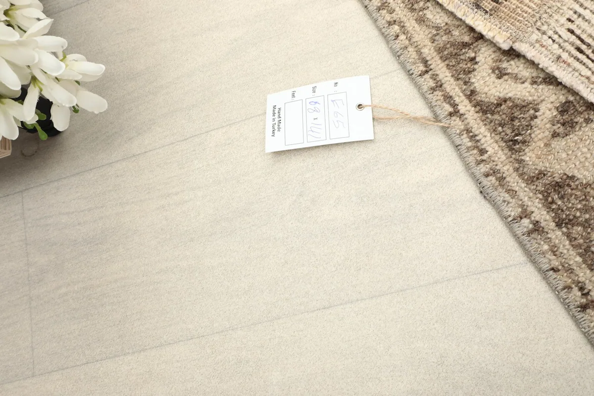 Corner of the rug with a care tag, showing the natural fringe and a light wood floor background