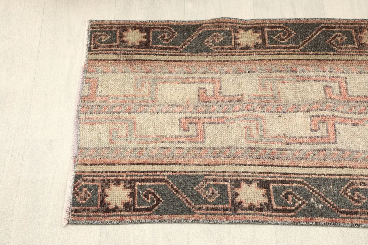 View of the rug's side border, featuring repeating charcoal and beige tribal designs.