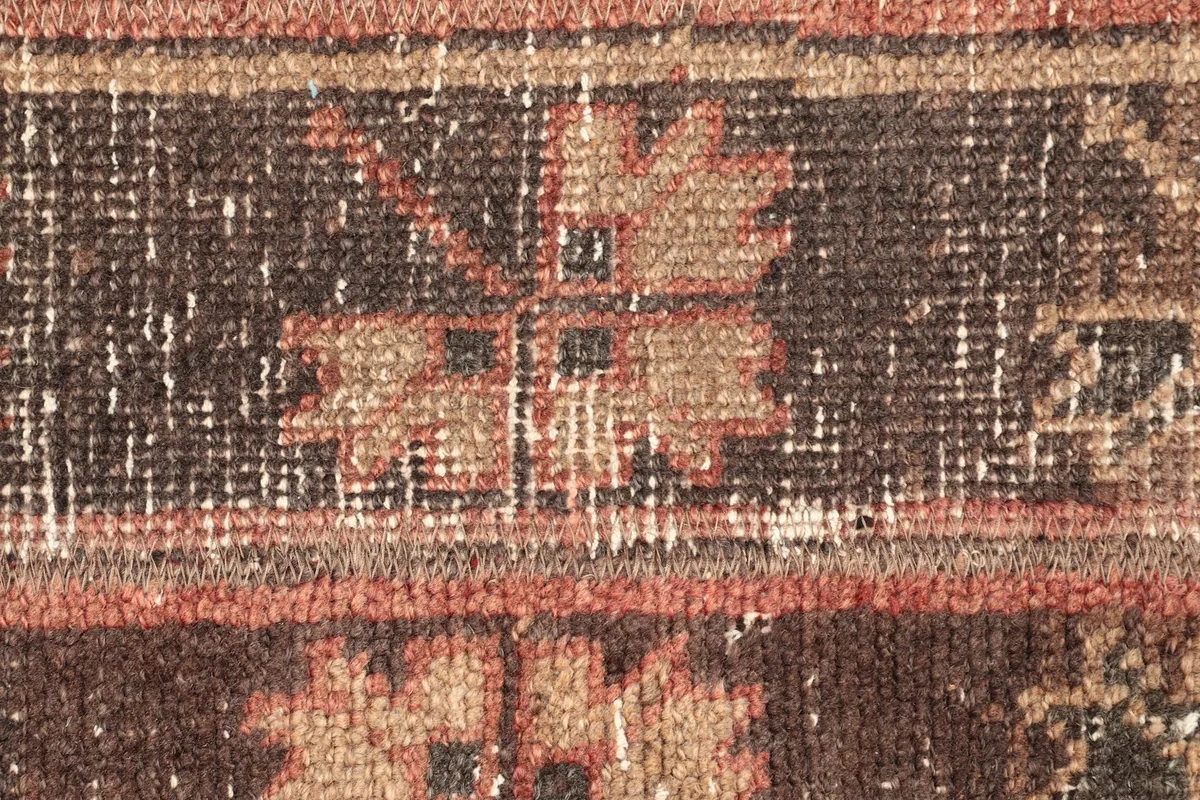 Macro detail of a geometric motif in rust and beige against the brown striped background.