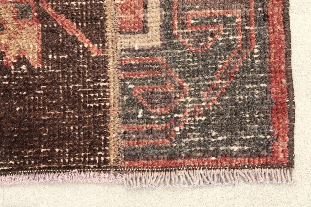 Close-up of the rug's edge, showing the low pile and intricate geometric patterns in gray and rust.