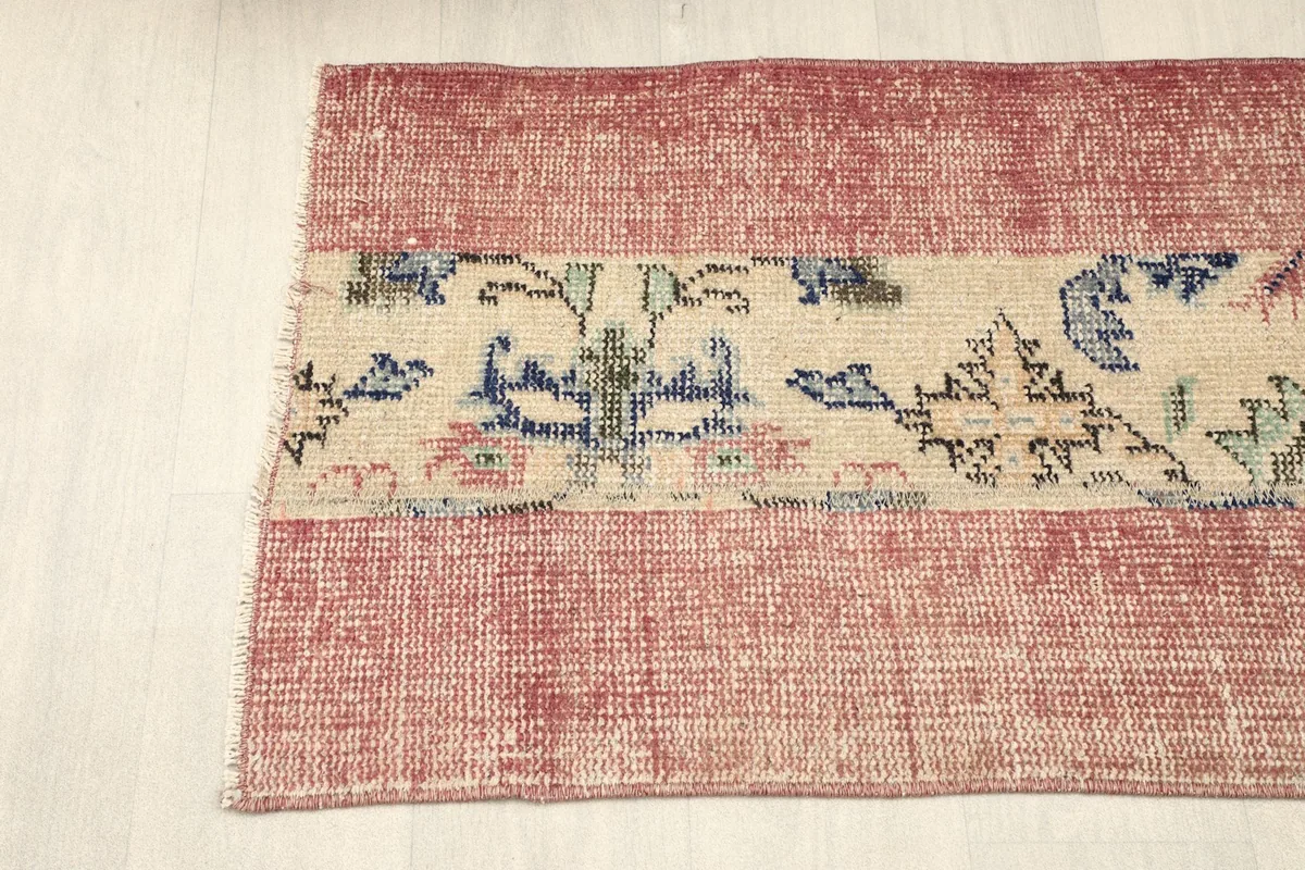 Top-down angled view of the left side of the rose and beige vintage area rug.