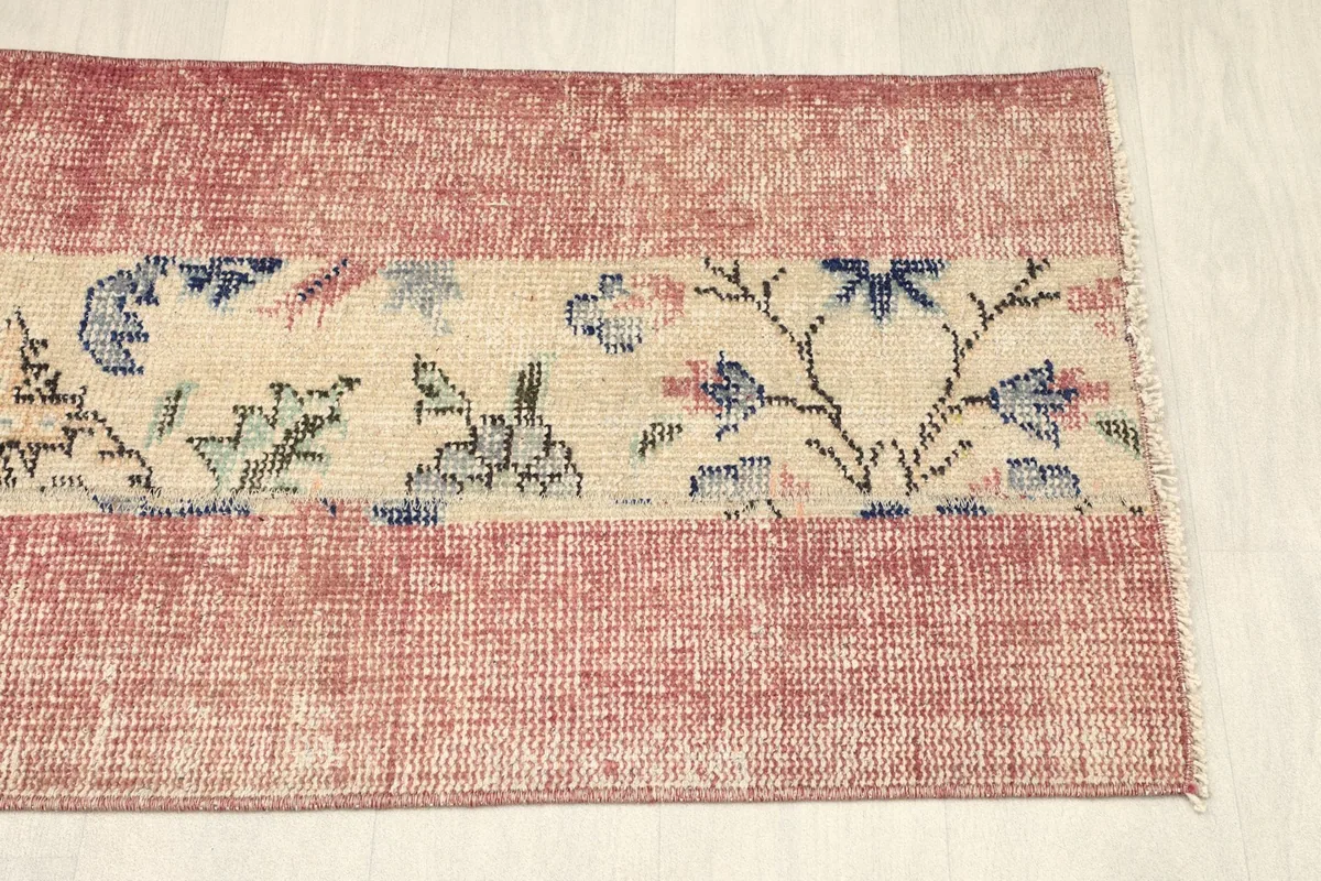 Top-down angled view of the right side of the rose and beige vintage area rug.