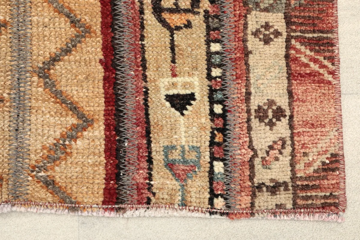 Close-up detail of the hand-knotted wool pile and fringe, showing the rust, tan, and gray colors.