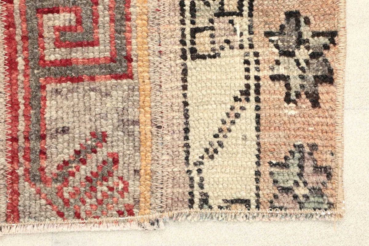 Close-up of the rug's surface, showing wool pile texture and geometric patterns in beige, red, and gray.