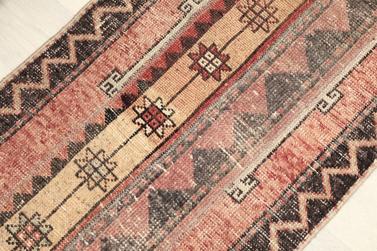 Angled view capturing the full length of the rug, emphasizing the central beige stripe and zigzag border.