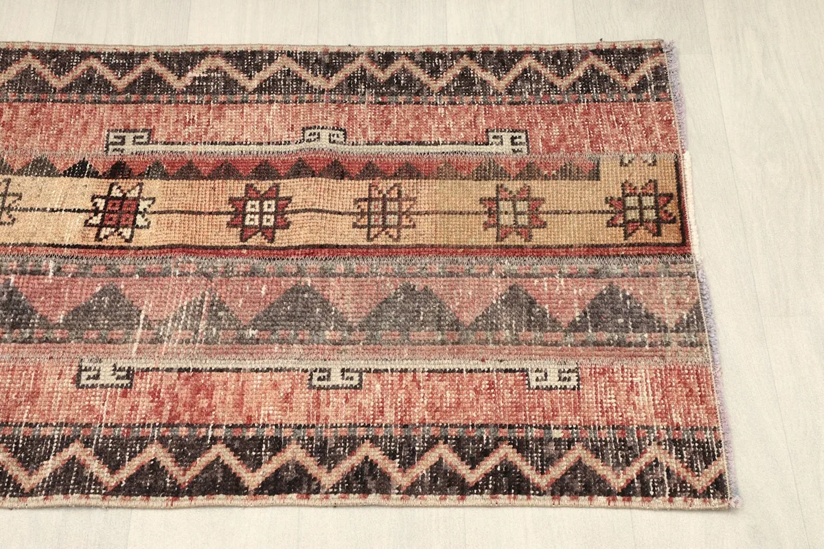 Partial angled view of the rug's bottom half, showcasing the distressed rose tones and tribal motifs.