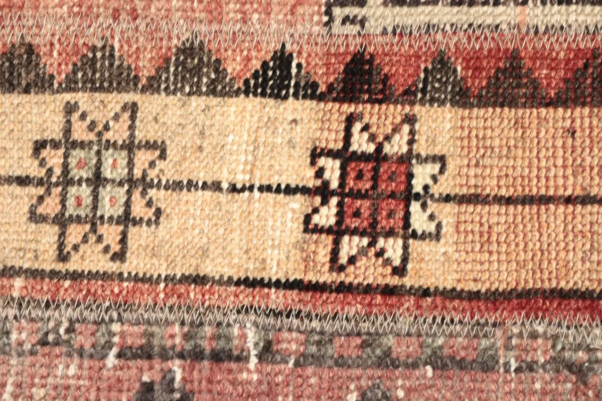 Macro detail of the geometric star motifs in red and charcoal within the beige central band of the rug.