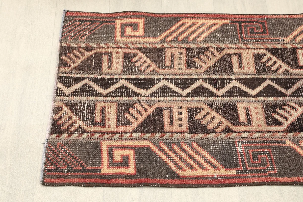 Close-up of the rug's left end, showing the distinct geometric motifs and the rust-colored border detail.