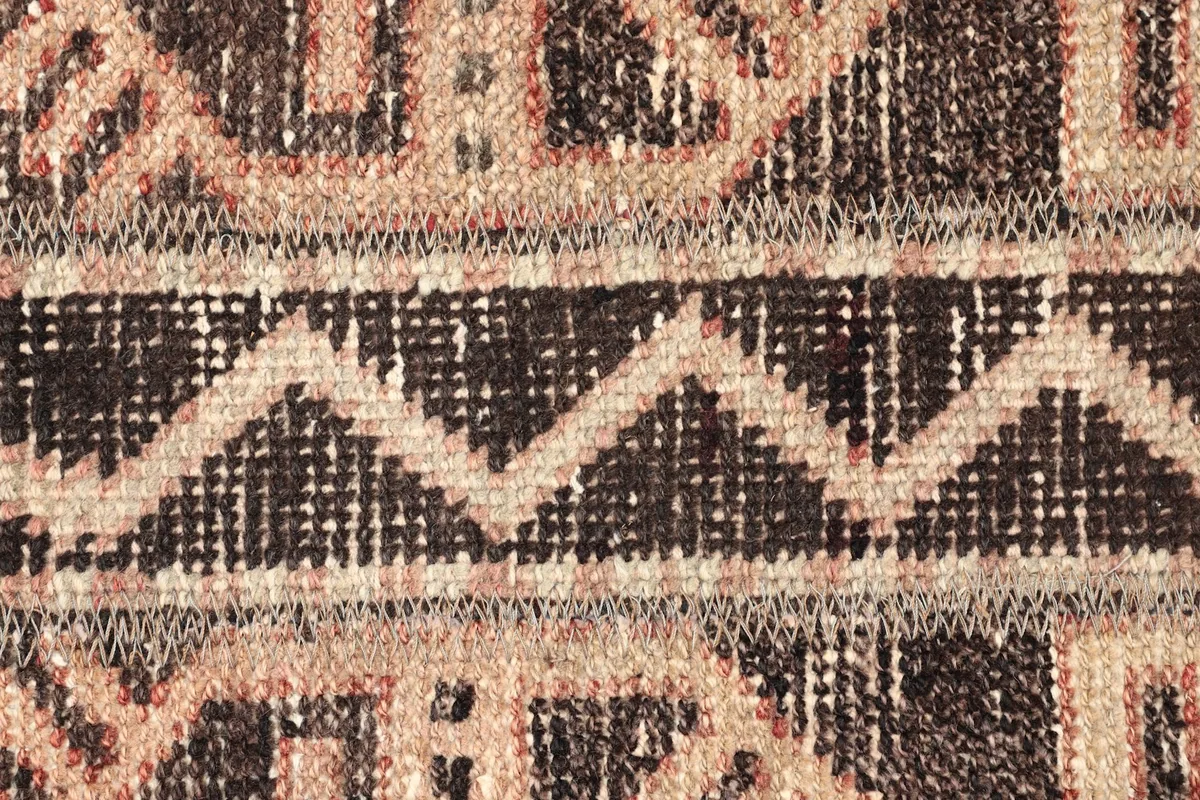 Detailed shot of the rug's low wool pile, revealing the intricate zigzag and hook patterns in brown and tan.