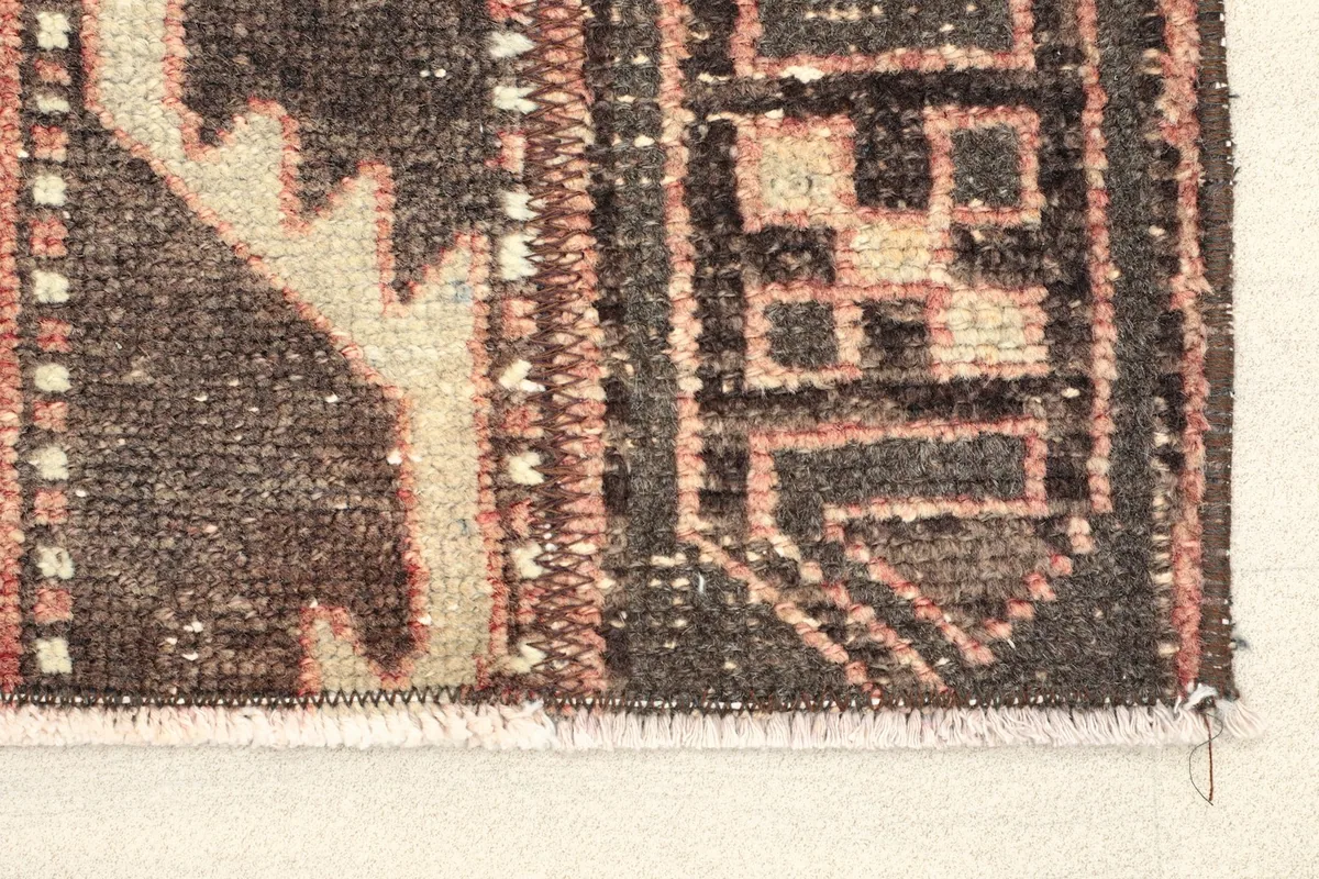 Close-up view of the rug's short fringe and a section of the dark brown geometric pattern