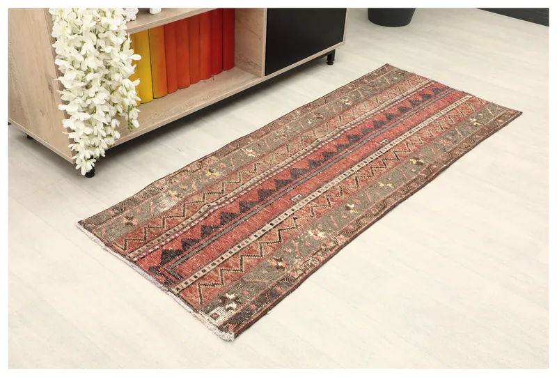 Full overhead view of the rust, brown, and gray tribal striped Anatolian runner rug on a white floor.