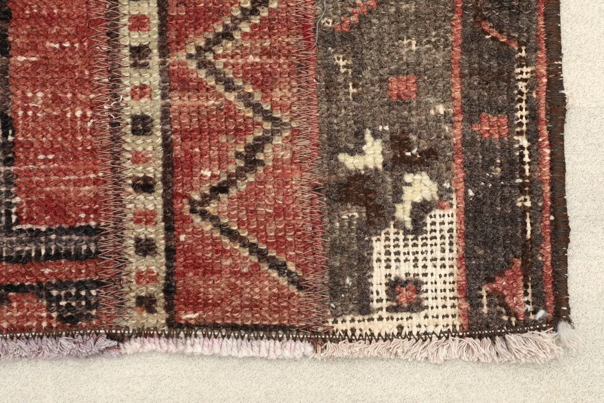 Close-up detail of the rug's end, showing the low pile, fringe, and intricate rust and black geometric motifs.