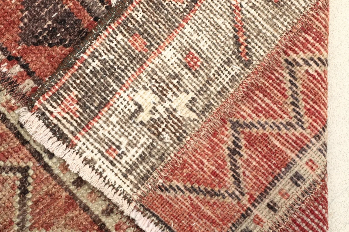 Detail of the rug's low pile and knotting structure, with visible wear and color blending.