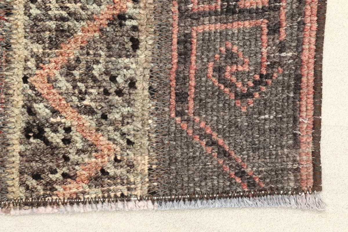 Close-up detail of the rug's edge, showing gray, rust, and beige geometric motifs and texture.