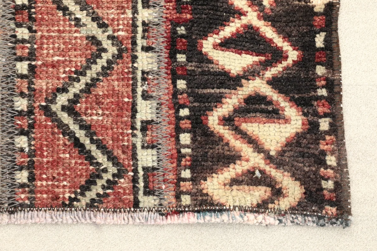 Close-up detail of the rug's end, highlighting the various rust, black, and ivory geometric patterns.