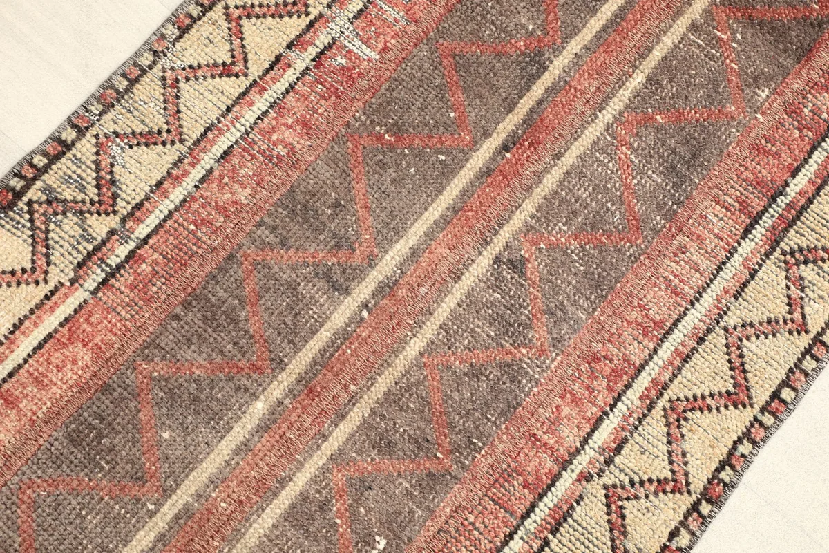 Angled view of the vintage rug, showing the blend of red, brown, and beige colors.