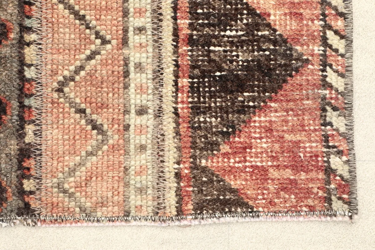 Close-up detail of the rug's edge, showing the rust and gray geometric patterns and hand-knotted texture.