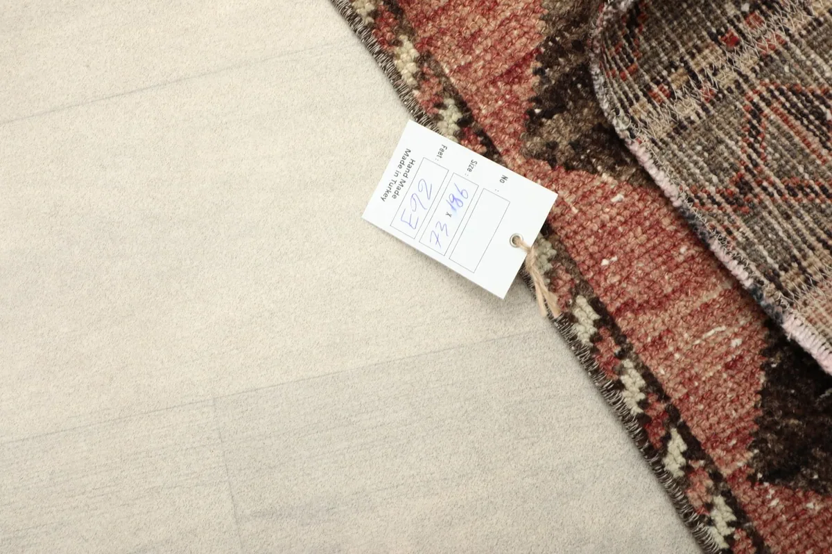 Corner of the rug with a tag, showing the wool pile and the hand-knotted detail on a white background.