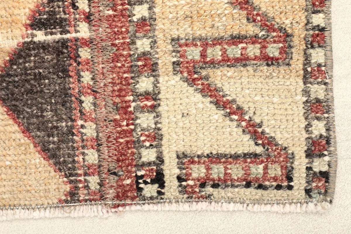 Close-up detail of the hand-knotted wool pile, showing beige, rust, and black geometric patterns