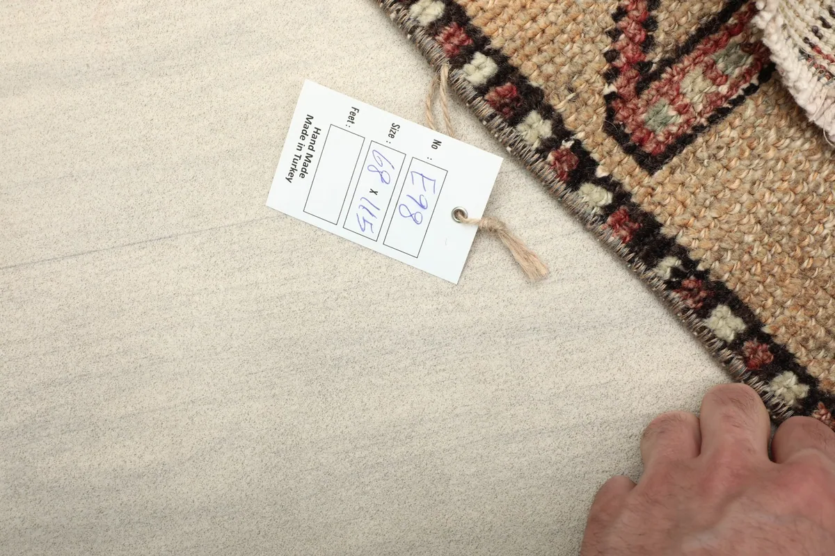 Hand pointing to the product tag with rug dimensions 68 x 115 cm, indicating its origin