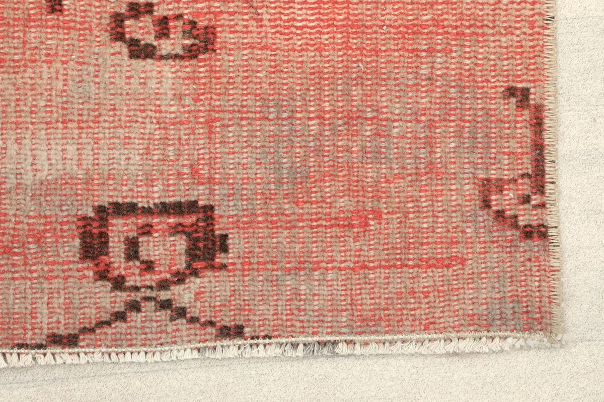Close-up detail of the rose wool pile and brown geometric motifs at one end of the rug.