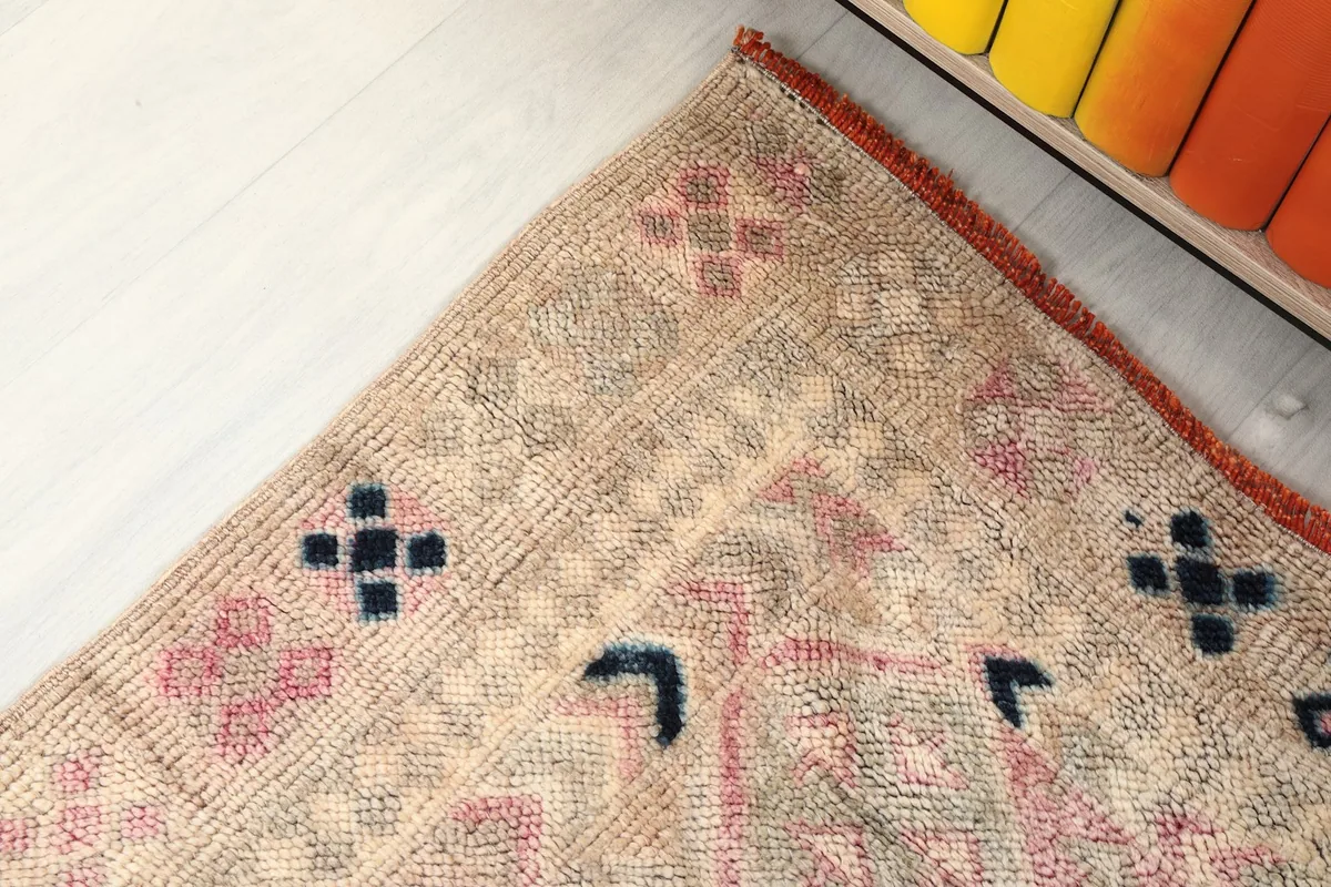Corner detail of the rug, revealing small black and pink motifs on the beige field