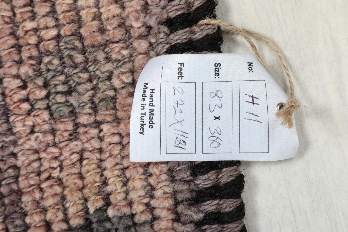 Close-up of the rug's pile with a size tag, confirming its dimensions and handmade origin.