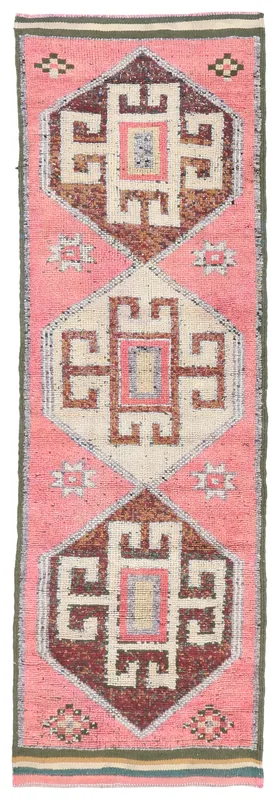 Full overhead view of a vintage pink, brown, and ivory tribal geometric Anatolian runner rug on a white background.