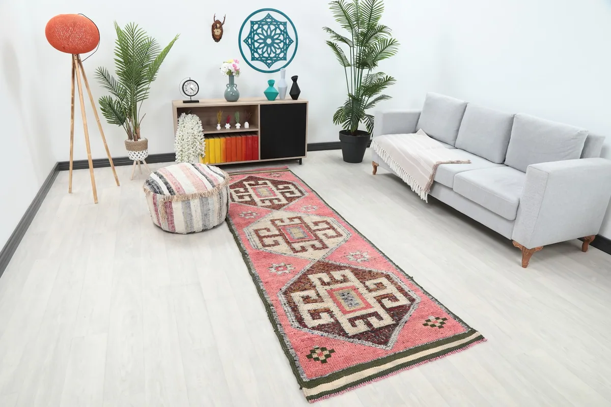 Angled view of the pink tribal geometric runner rug in a room, showing its length beside a sofa.