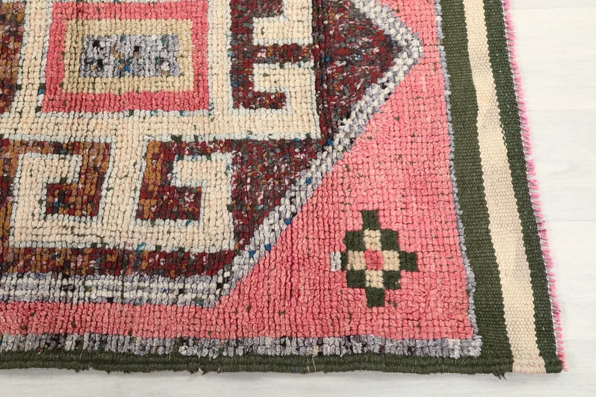 Detailed view of the pink field, brown and ivory geometric patterns, and the olive green border of the runner.