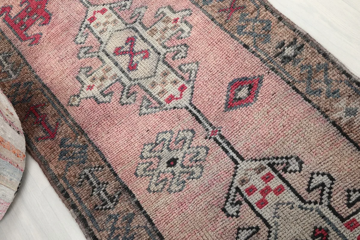 Angled view highlighting the faded rose color and intricate geometric designs of the hand-knotted rug.