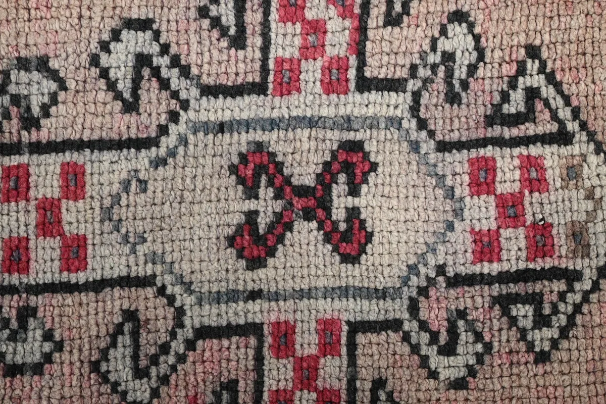 Close-up of a central tribal geometric motif in rose, gray, and black on the rug's field.