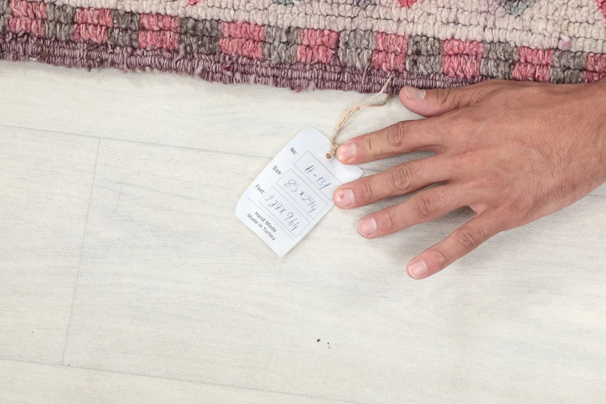 A hand next to the product tag, showing the rug's details and scale