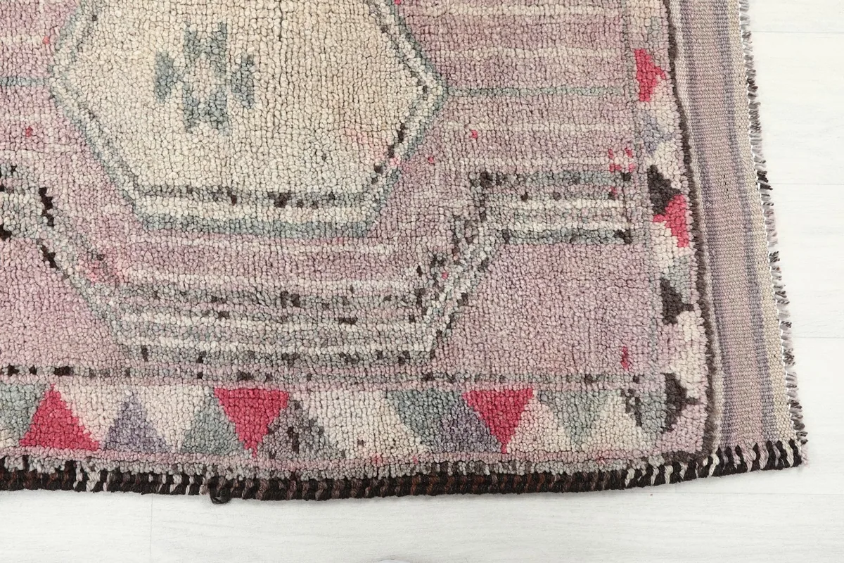 Detailed view of the rug's geometric pattern and border, showing rose, ivory, and red tones.