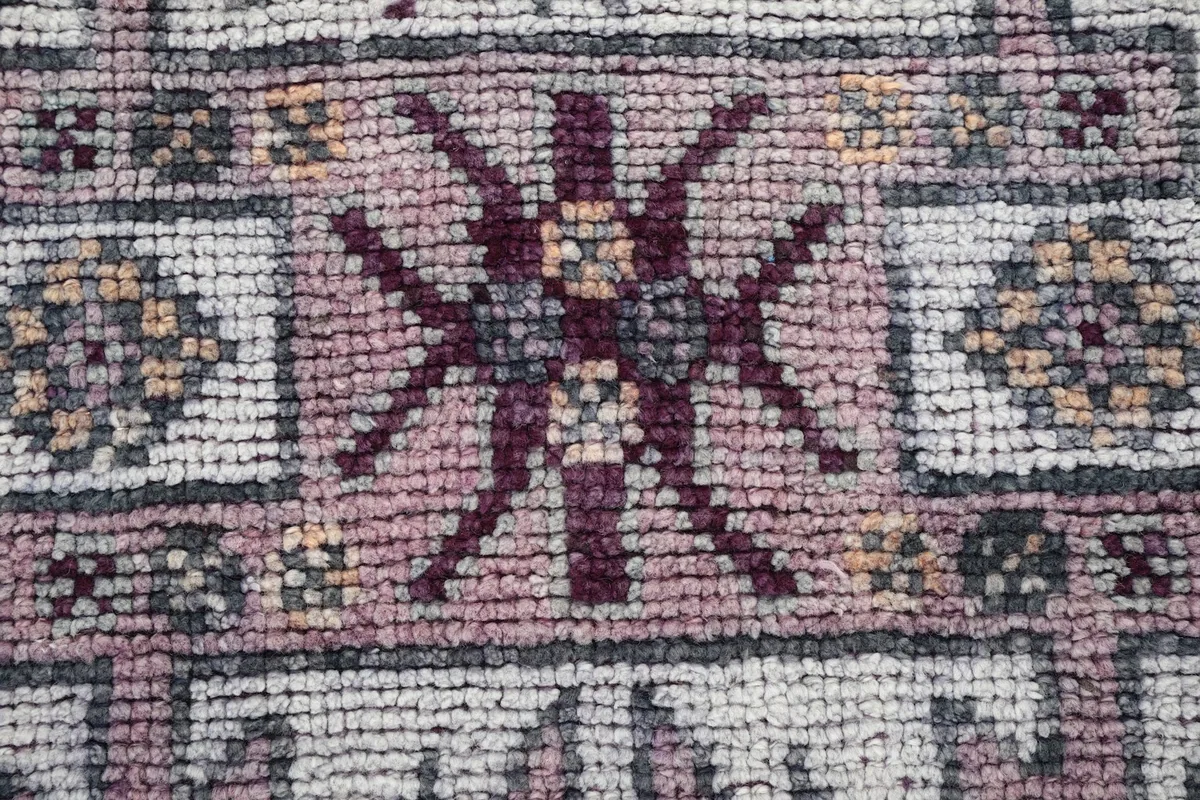 Extreme close-up of a central medallion motif, showing the texture of the wool pile and purple hues.