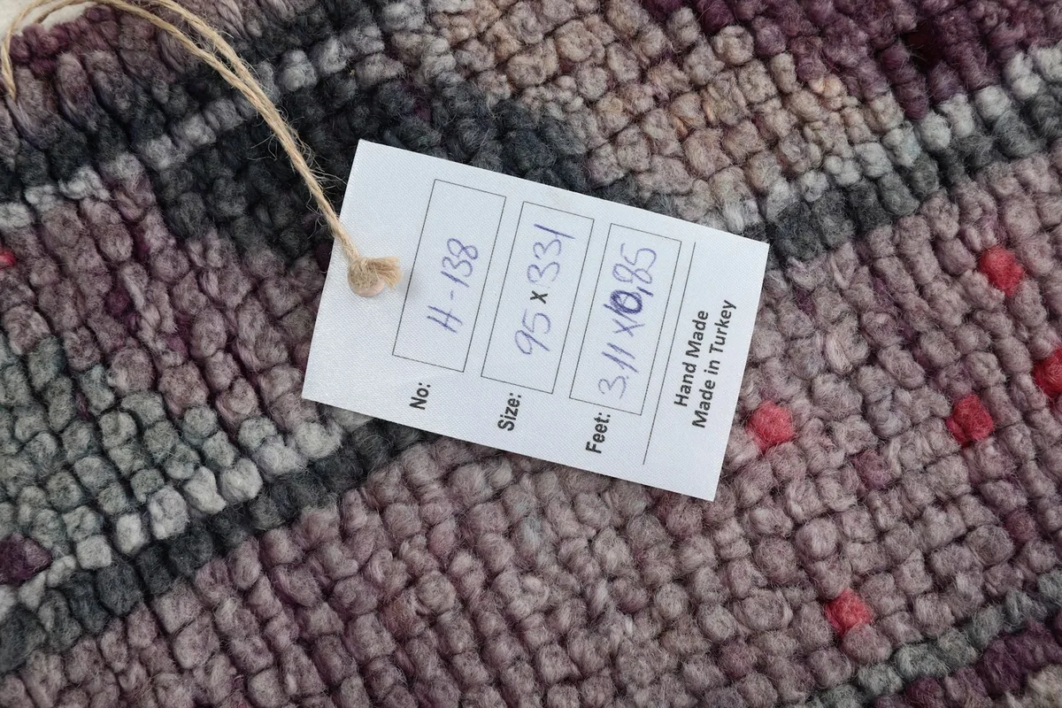 Product tag on the rug, indicating it is hand-made in Turkey with dimensions 95 x 331 cm.