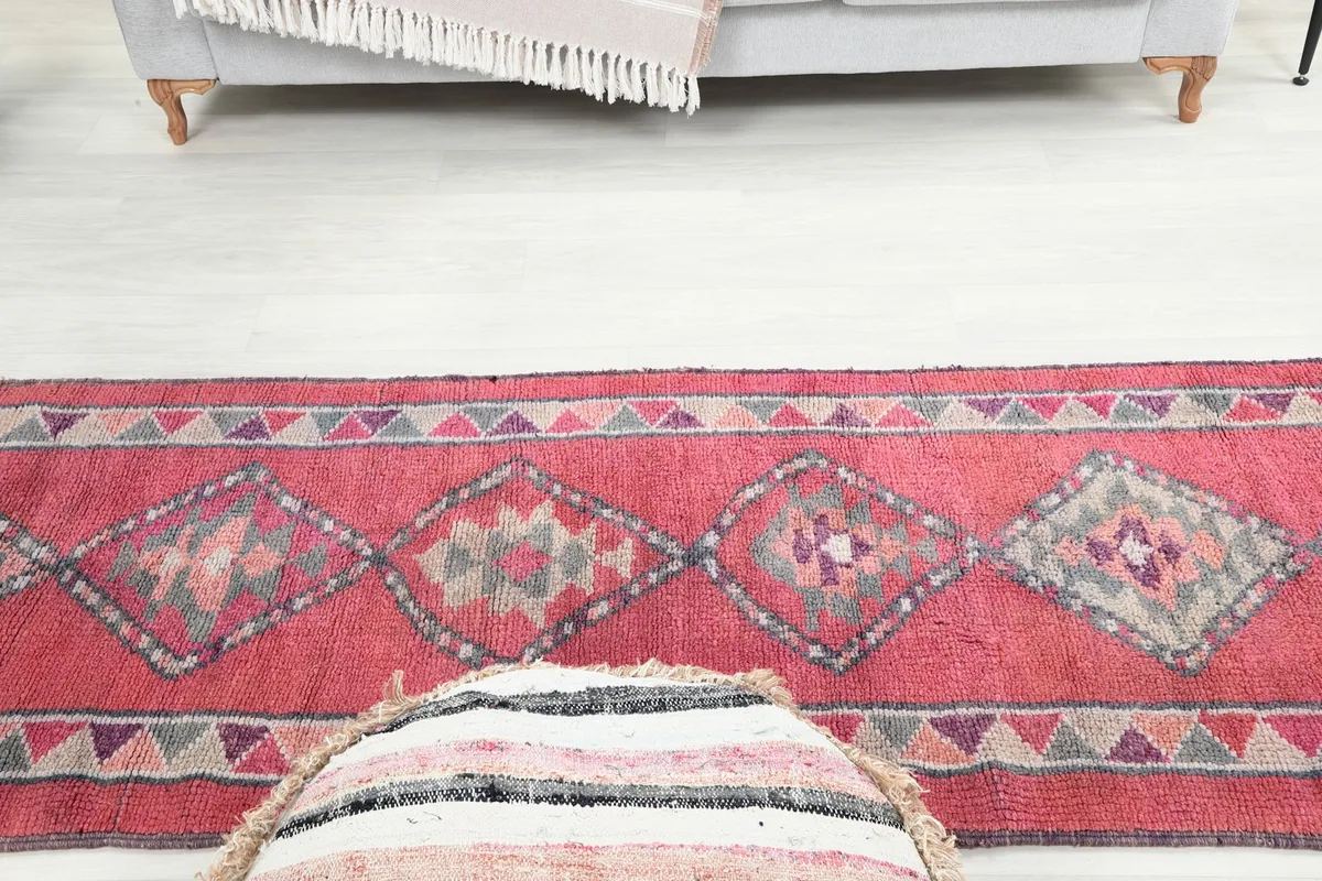 Angle view of the rose runner rug's patterns and colors, with a pouf in the foreground and a sofa in the background.