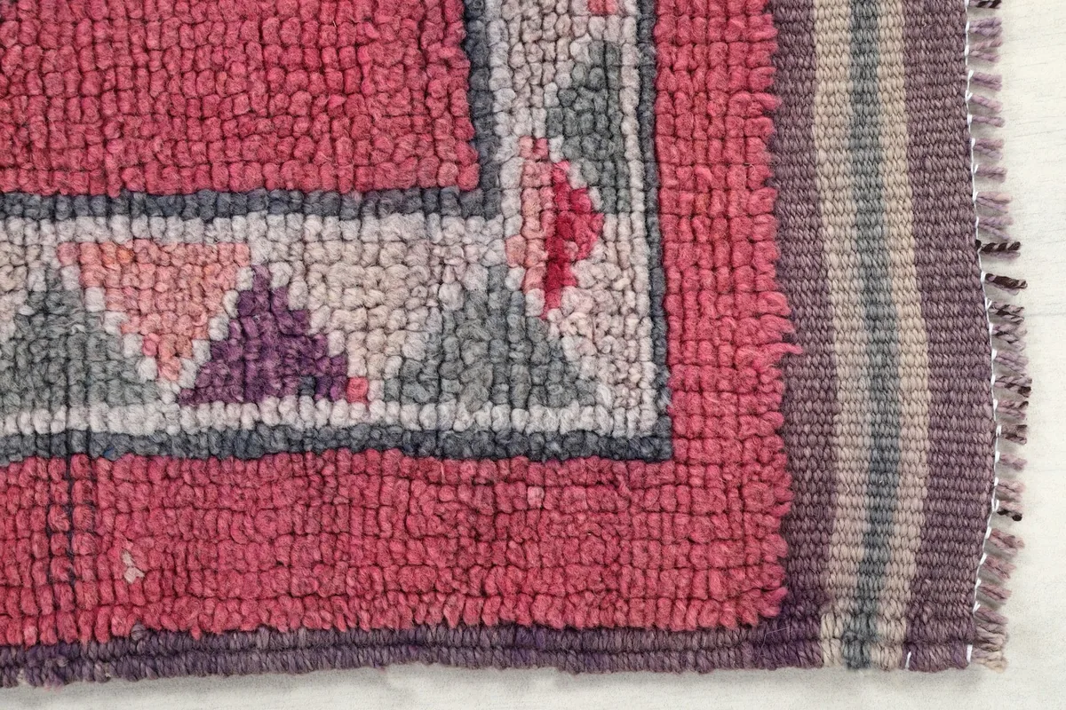 Detail of the rug's border, showcasing the hand-knotted wool pile and triangular patterns in rose, gray, and purple.