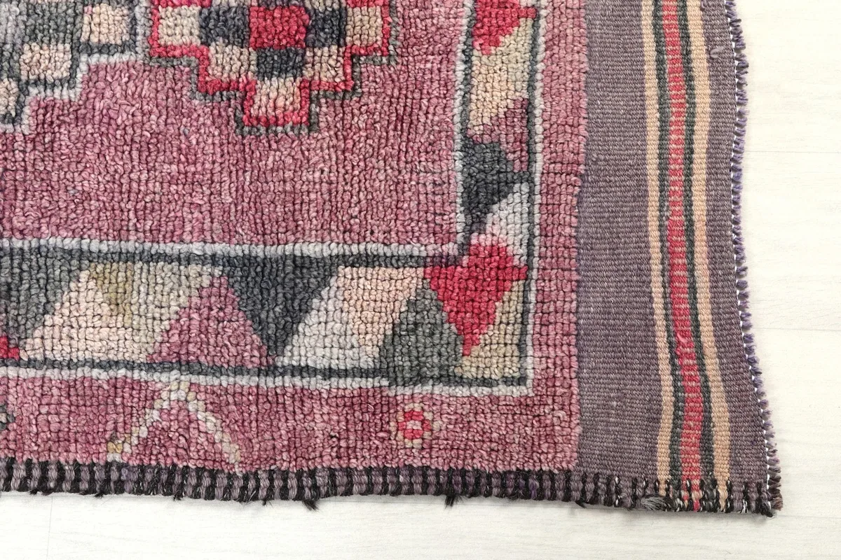 Detailed view of the rug's end, showing the rose field, geometric border, and fringe